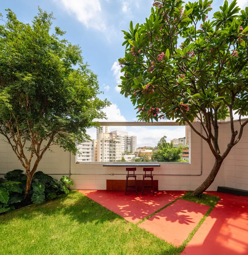 Rooftop terrace with red floor, planted trees, and horizontal window framing the urban skyline beyond