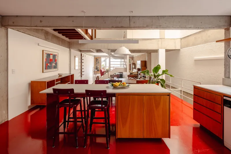 Kitchen island with wood base on glossy red epoxy floor beneath concrete beams and a skylight