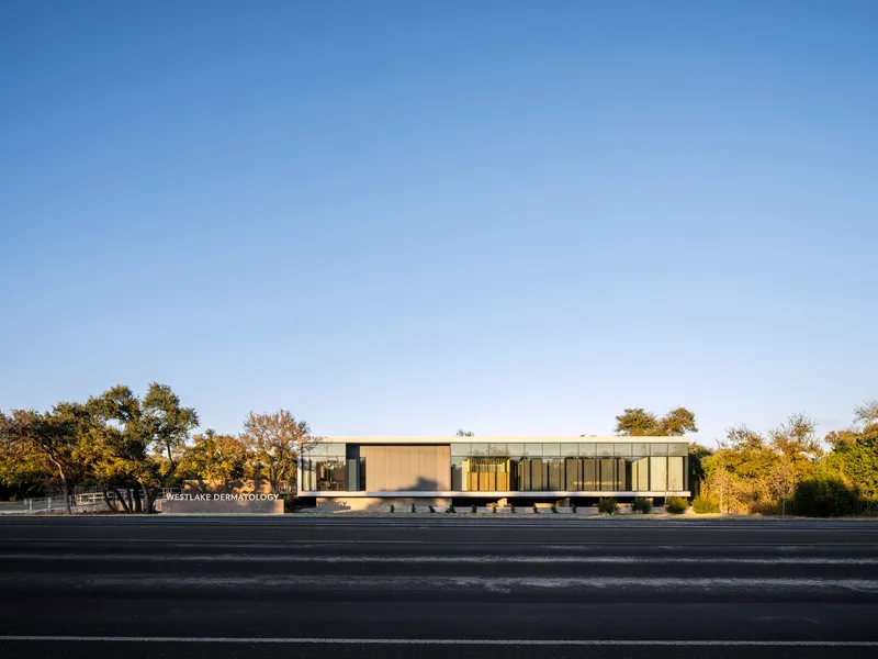 Street view of the horizontal facade showing vertical metal panels and glazing with mature trees beyond