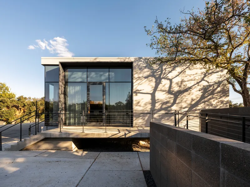 Rear elevation showing the glass corner with tree shadows falling across the white panel facade