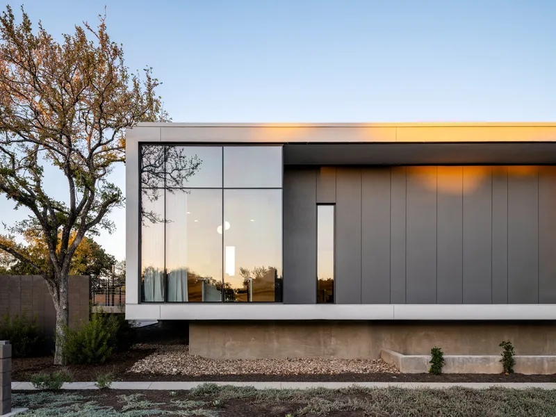 Facade corner at dusk with corner glazing and vertical metal cladding above a concrete plinth base