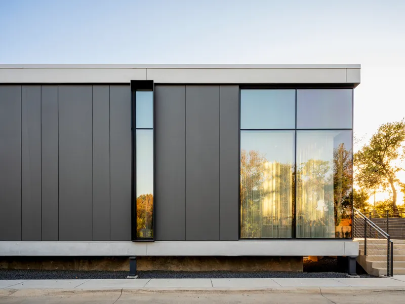 Dark metal panel facade with narrow vertical window and large glass opening at dusk