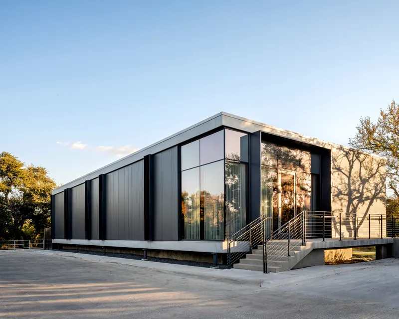 Corner view showing glass curtain wall and concrete entry stairs with metal railings at sunset