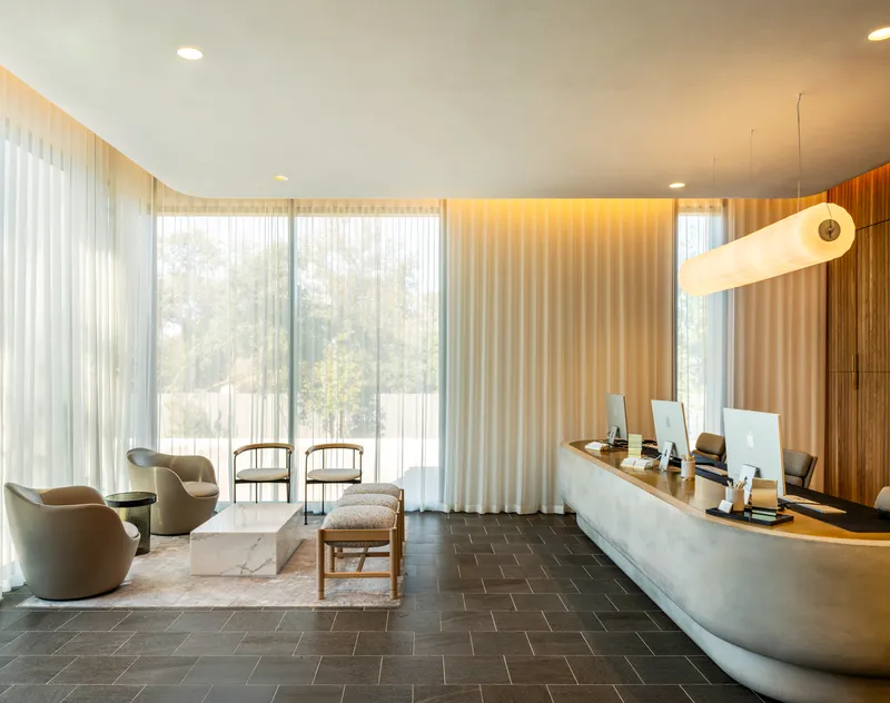 Reception area with curved desk, dark herringbone floor and floor-to-ceiling sheer curtains