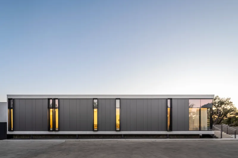 Street facade with dark metal panels and vertical window slits illuminated at dusk