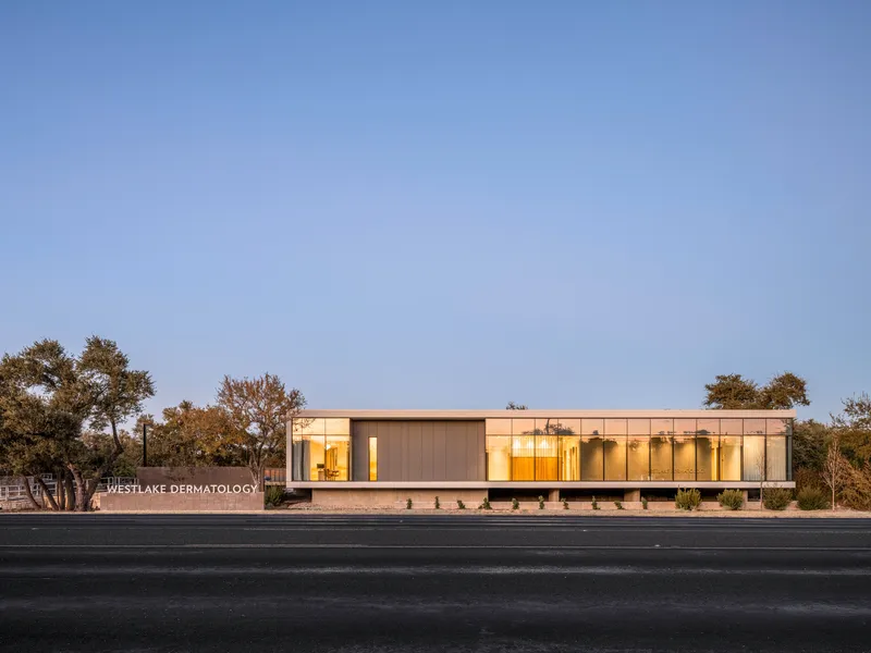 Front elevation showing the low horizontal volume with illuminated interior at dusk
