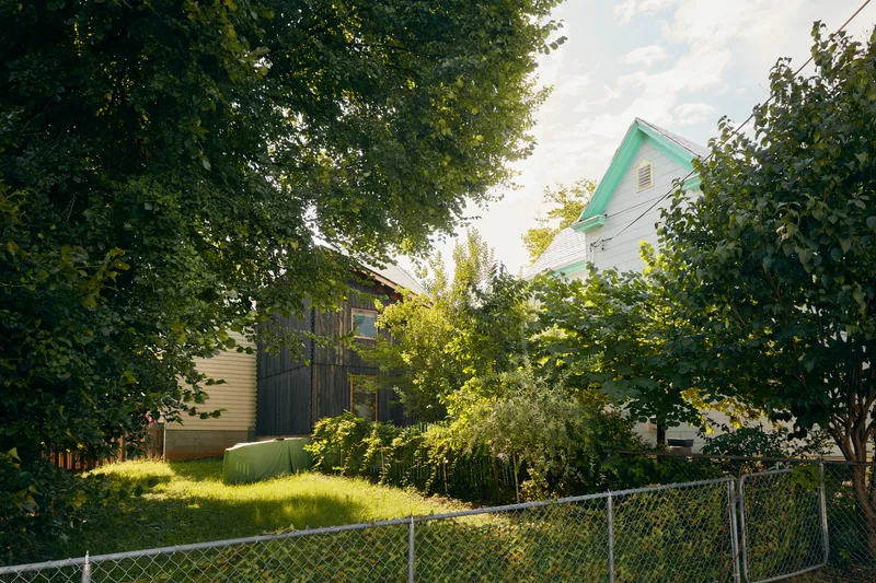 Garden view of the dark wood structure between a mint green house and surrounding deciduous trees