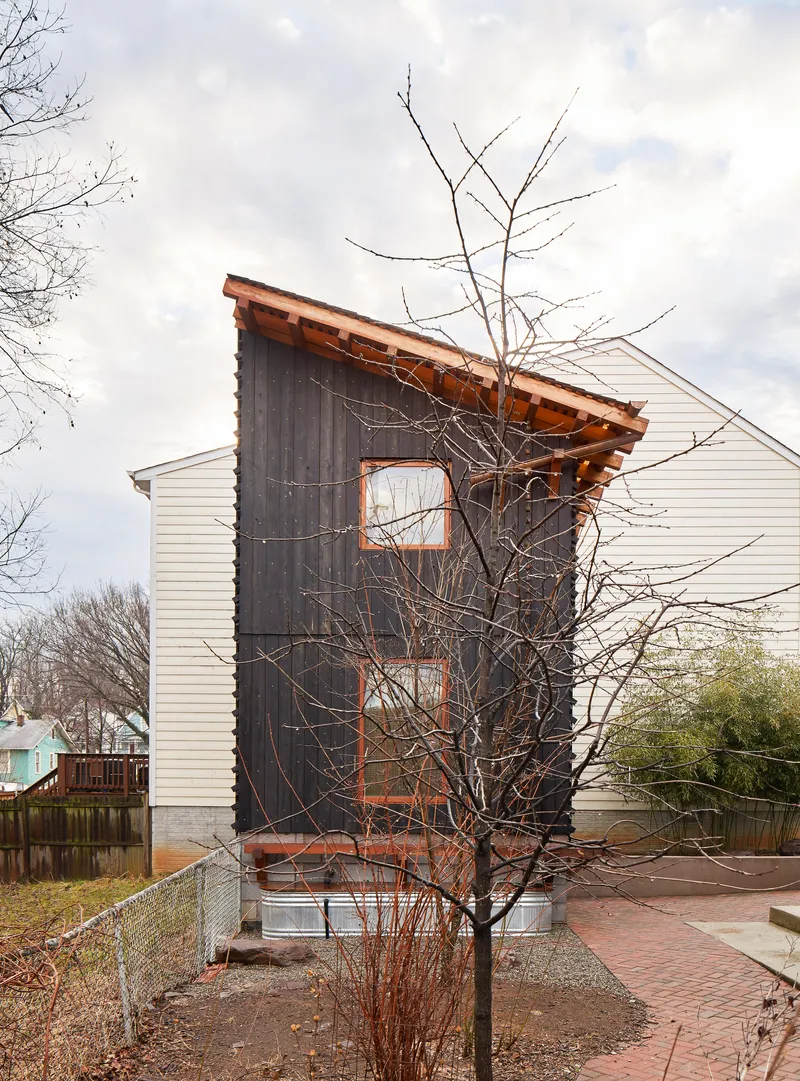 Charred timber facade with white horizontal siding addition beside a bare winter tree