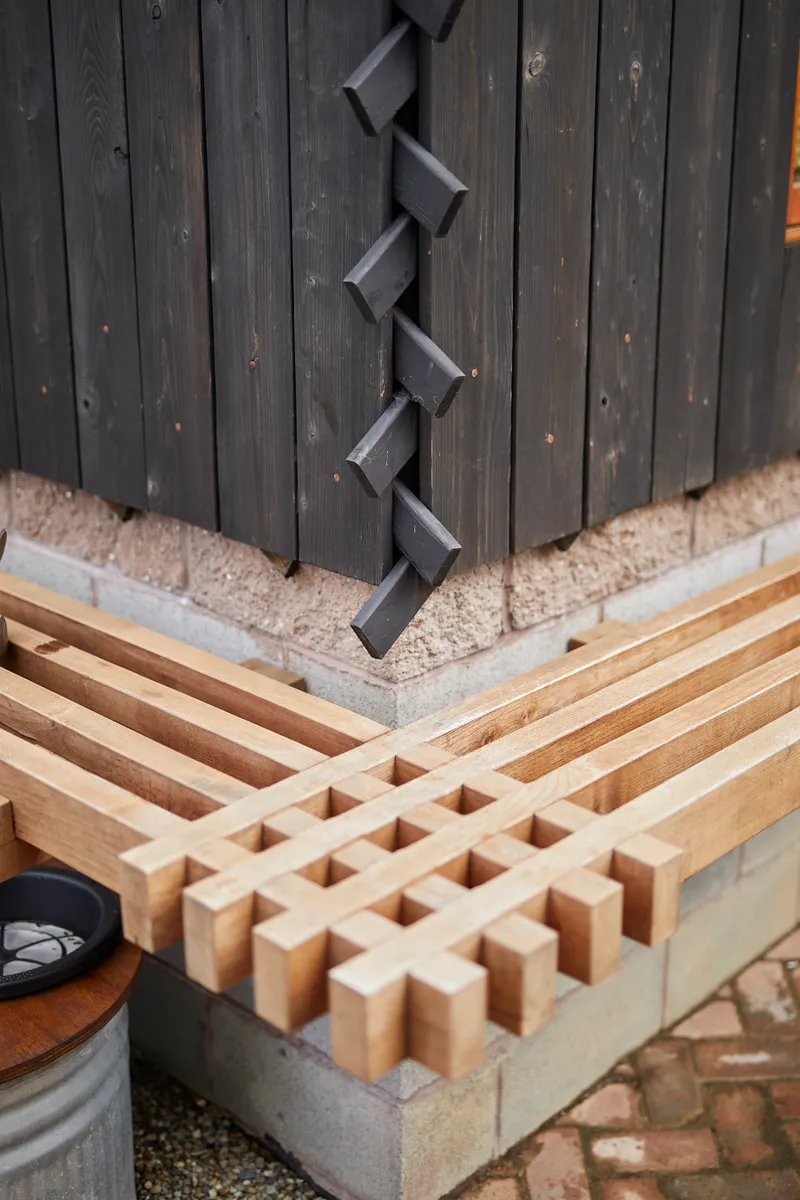 Corner detail showing charred vertical boards meeting a timber gridded bench on a concrete base