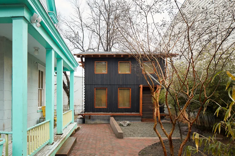 Two-story dark timber-clad volume with square windows seen from a turquoise porch across bare trees