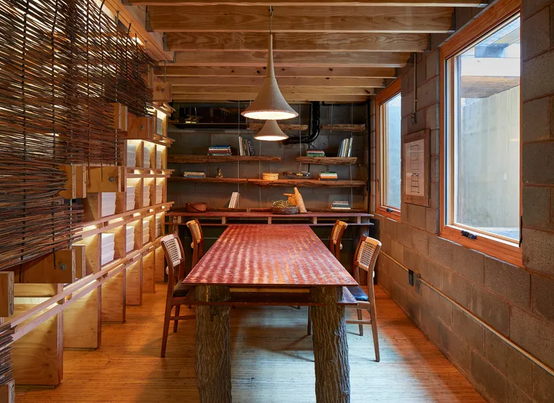 Dining room with exposed timber ceiling beams, horizontal wood shelving and woven screen partition wall