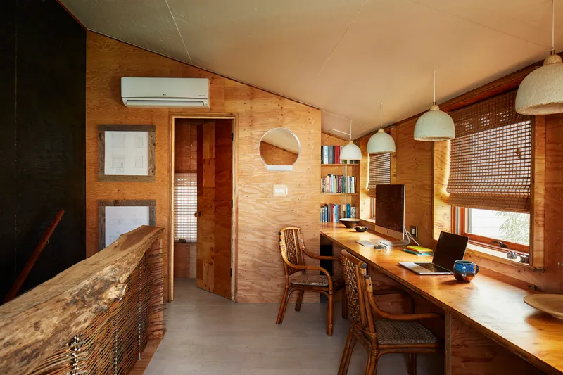 Study area with plywood walls, built-in desk and woven lattice window shades in afternoon light