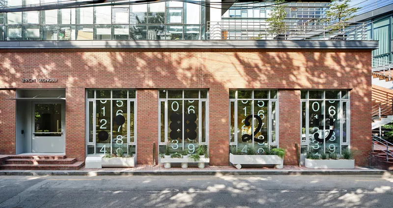Red brick facade with tall windows overlaid by white numeric patterns and dappled tree shadows