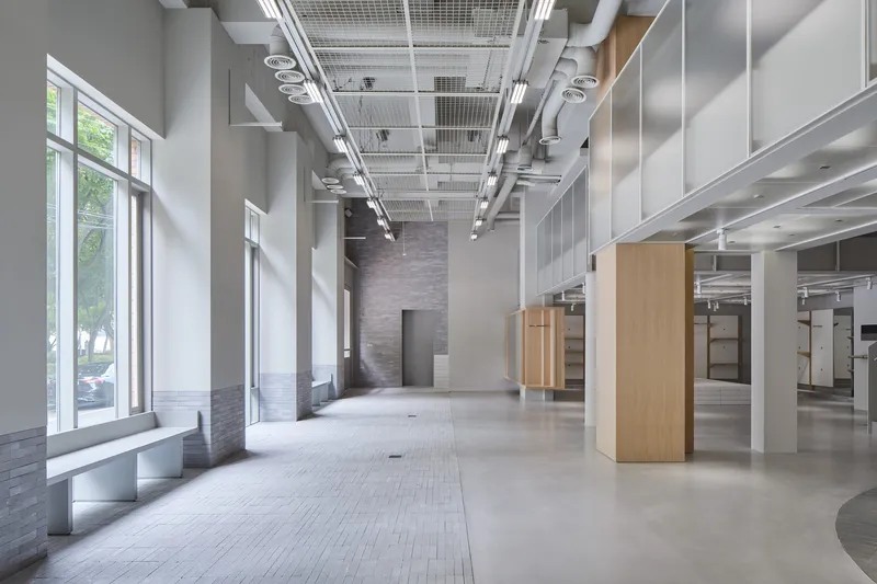 Open ground floor interior with floor-to-ceiling windows, exposed ceiling grid, and timber columns
