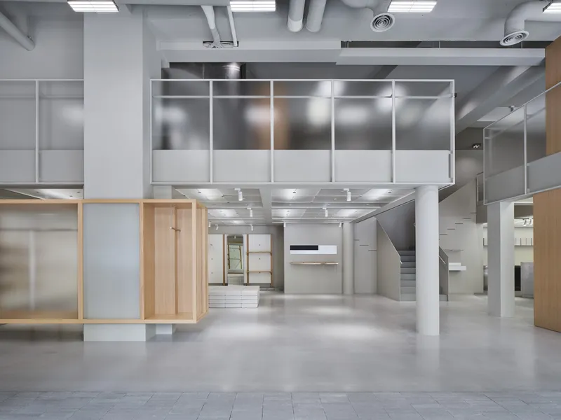 Open floor retail interior with hanging mezzanine, light wood display units, and exposed ceiling ducts and lighting
