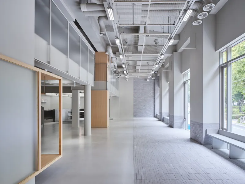 Circulation corridor with exposed mechanical ceiling, timber-framed display boxes, and daylight from streetside windows