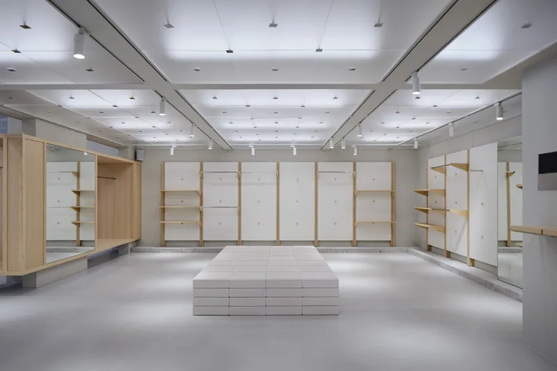 Retail interior with timber and white panel shelving units around a central platform under track lighting