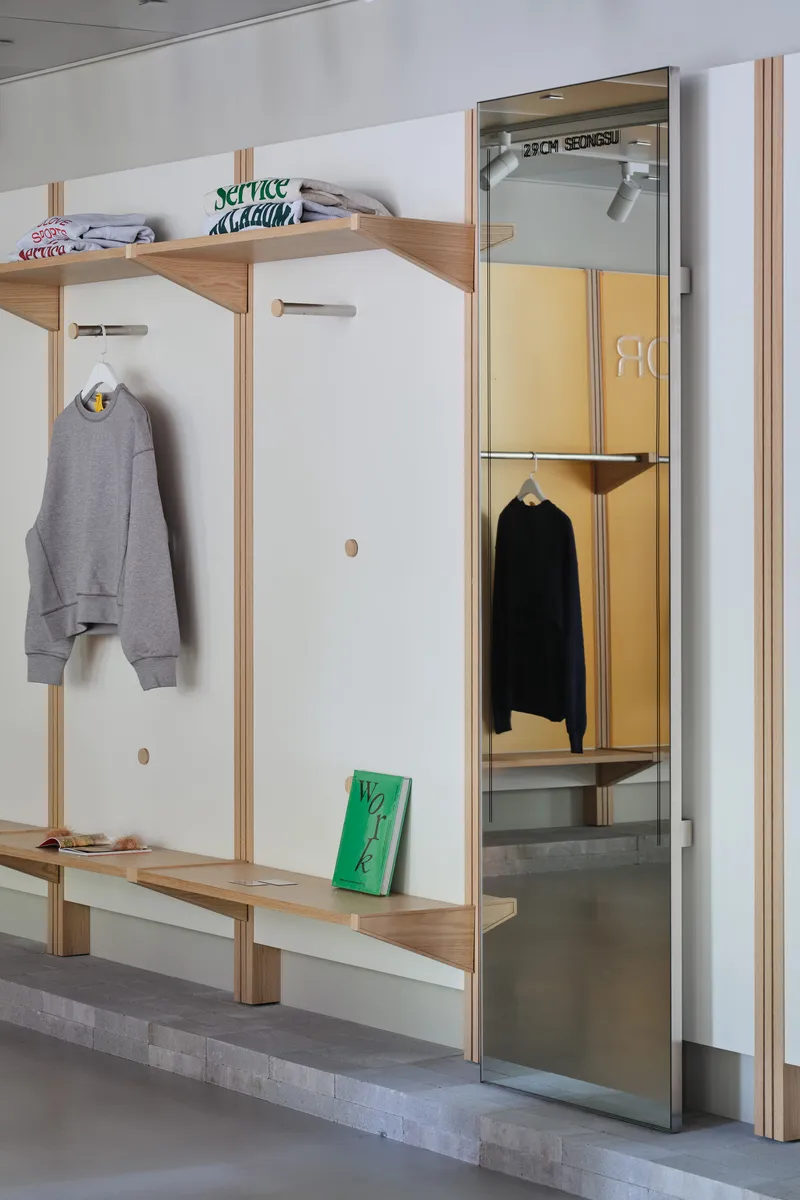 Detail of timber shelving unit with white panels, hooks, and a glass door revealing a yellow interior