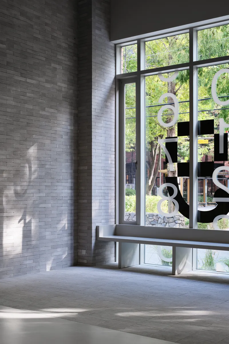 Grey brick wall beside a full-height window with graphic signage overlooking a sunlit courtyard