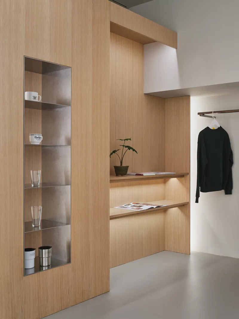 Light wood millwork featuring recessed shelving with a potted plant and hanging garment