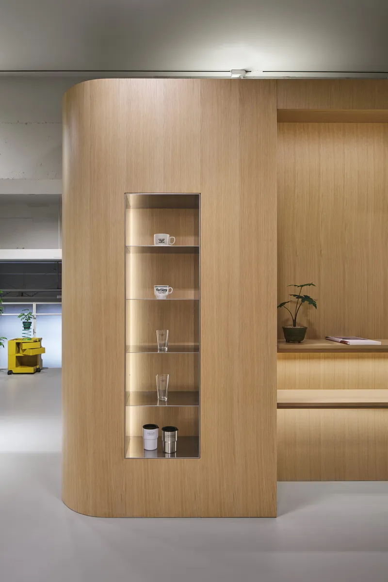 Curved light wood volume with vertical display niche containing glassware and ceramics