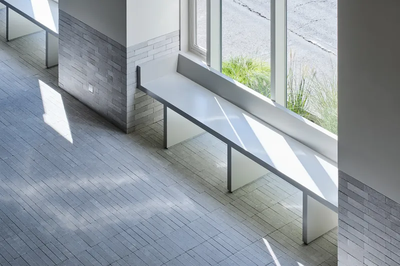 White metal bench with glass balustrade beneath tall windows letting in bright afternoon sunlight
