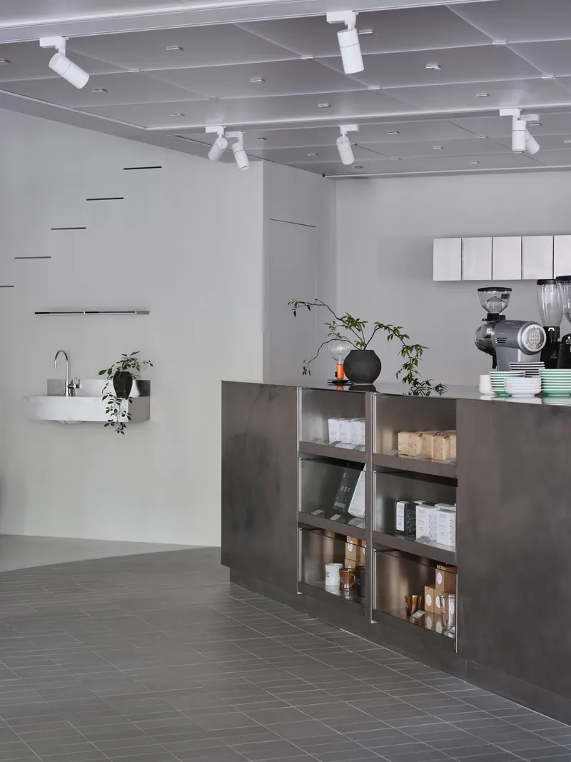 Open service counter with dark metal cabinetry and open shelving displaying coffee equipment and plants