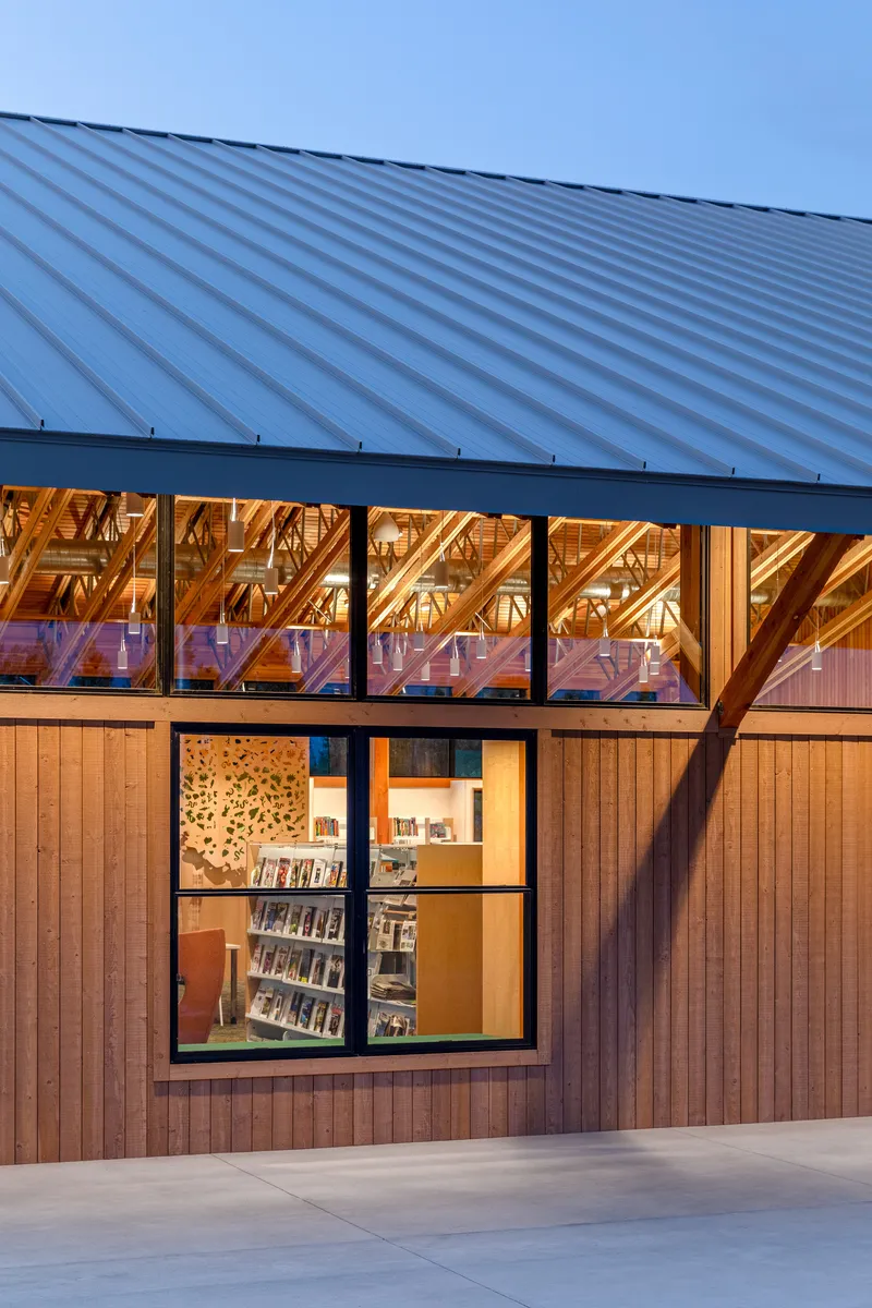 Close-up of metal standing seam roof above clerestory glazing revealing diagonal timber bracing at twilight