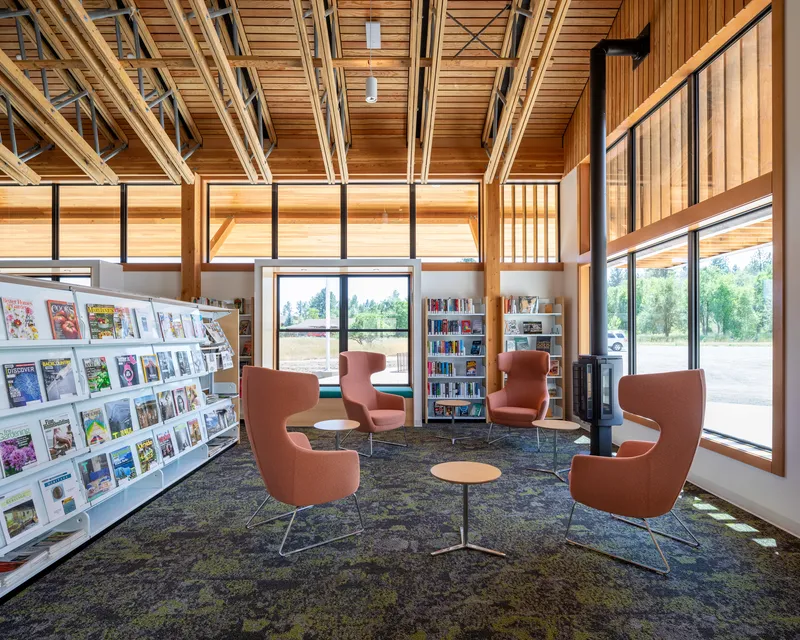 Reading area with terracotta upholstered chairs arranged around low tables beneath a timber ceiling structure