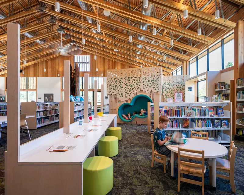 Open-plan library space with exposed timber trusses, clerestory windows, and children using reading tables