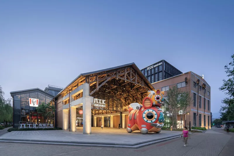 Timber truss pavilion with concrete columns and a painted mascot sculpture at the entrance plaza