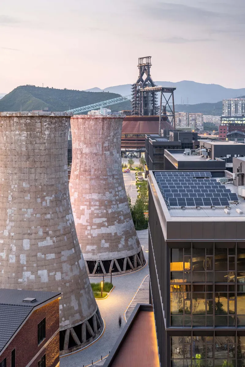 Preserved brick industrial chimneys beside rooftop solar panels and a steel headframe against distant mountains