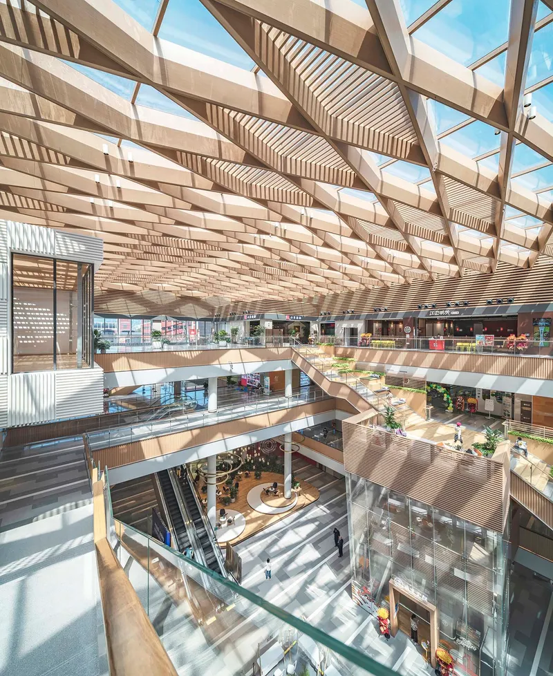 View down through the layered timber-screened balconies and central atrium beneath the latticed skylight
