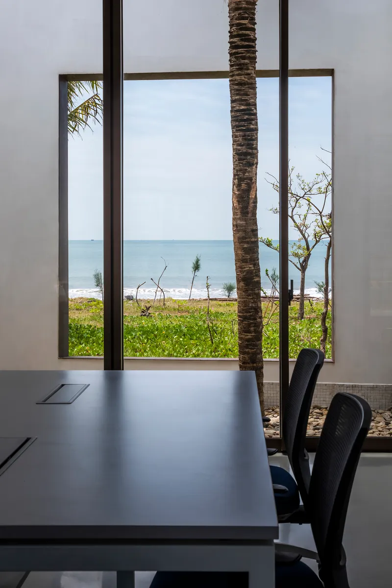 View through floor-to-ceiling window framing a palm tree trunk with ocean horizon beyond