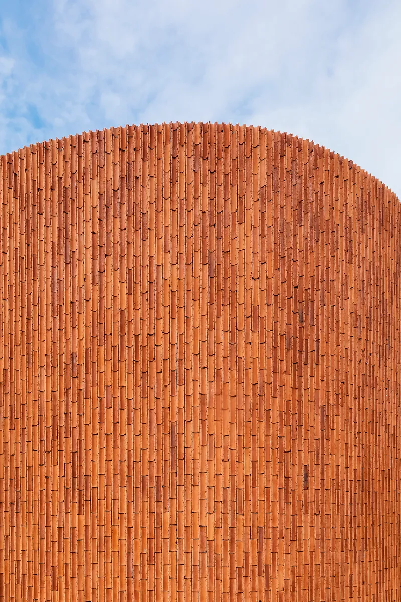 Curved terracotta brick facade rising against a partly cloudy sky