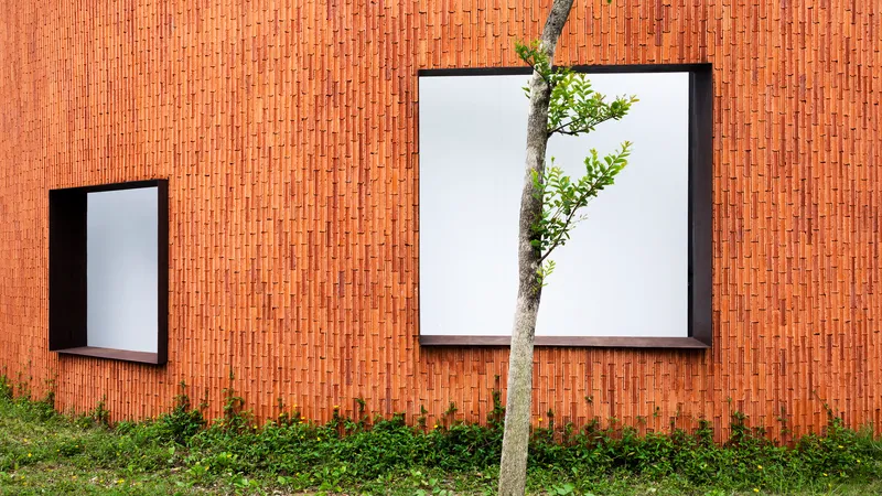Close view of the terracotta brick wall with black-framed windows and a young tree