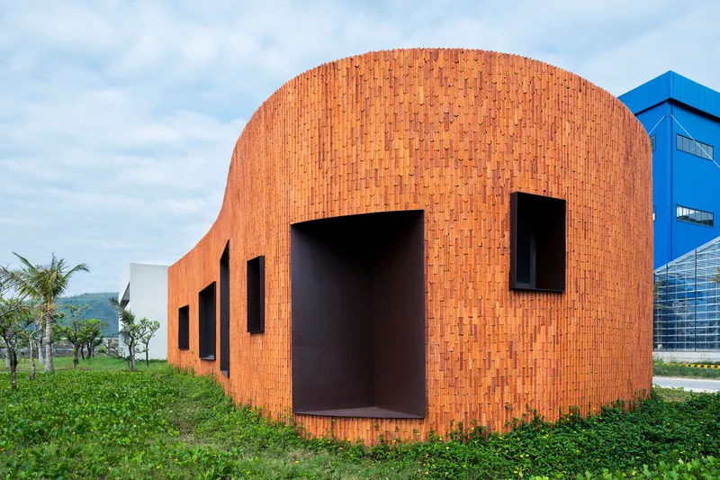 Curved brick facade with deep-set rectangular openings in a grassy field under cloudy skies