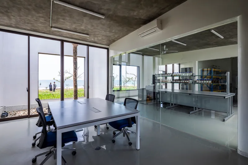 Interior workspace with glass partition separating meeting area from stainless steel equipment beyond full-height glazing