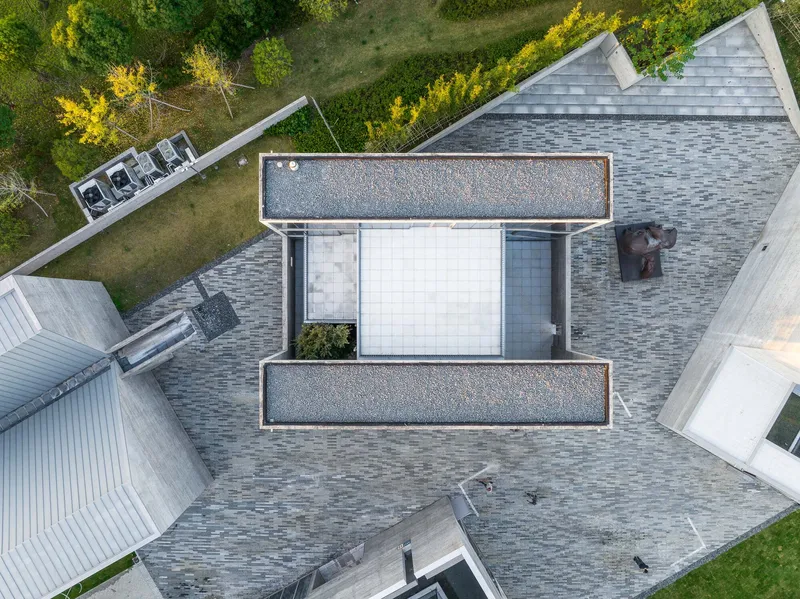 Aerial view of tiled roof with white skylight canopy and gravel-filled terrace surrounded by autumn trees