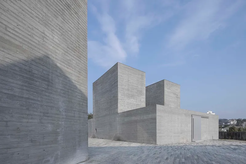 Stepped concrete volumes with horizontal board-formed surfaces under an overcast sky