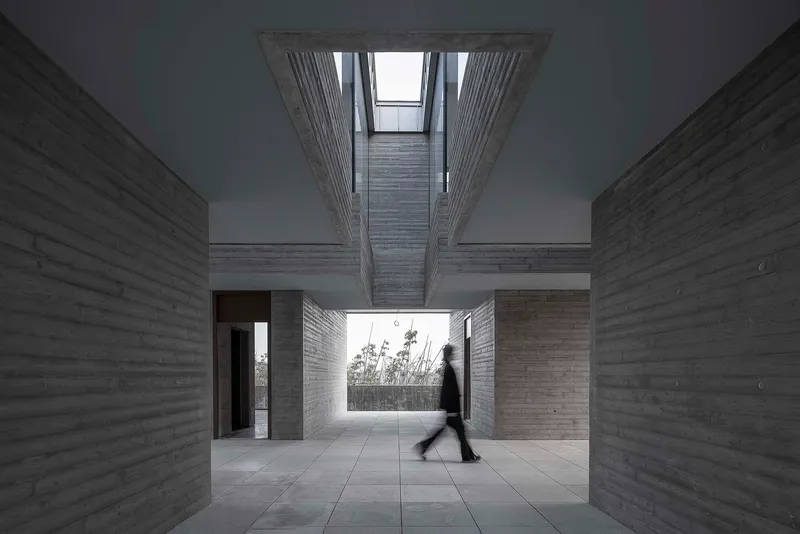 Interior courtyard with board-formed concrete walls, open skylight above, and a person in motion