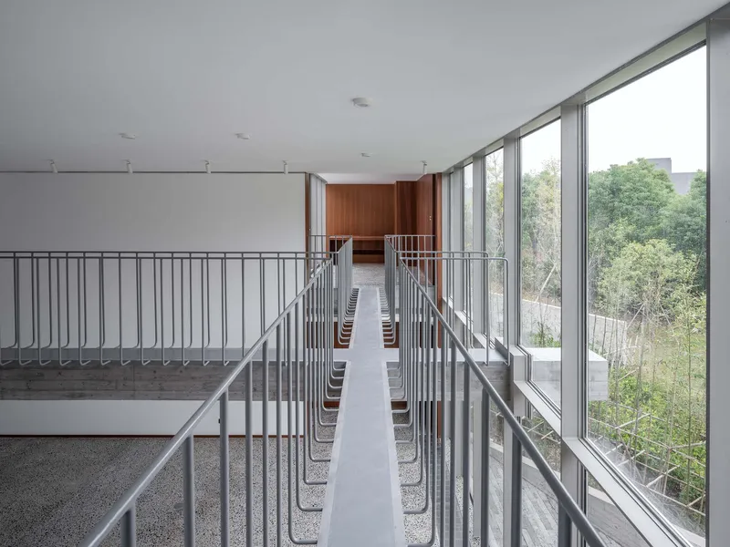 Narrow interior bridge with metal handrails and rows of seating leading toward timber-clad volume