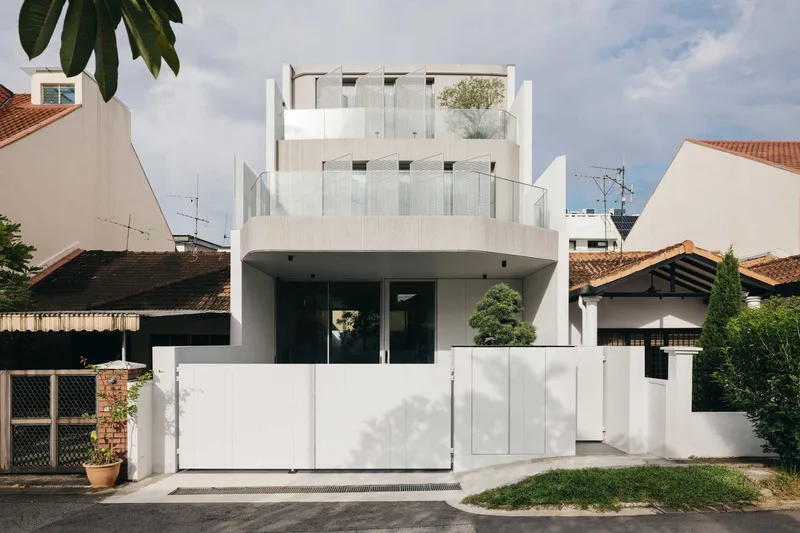 Street facade of a white multi-story residence with stacked balconies and glass railings among tiled-roof neighbors