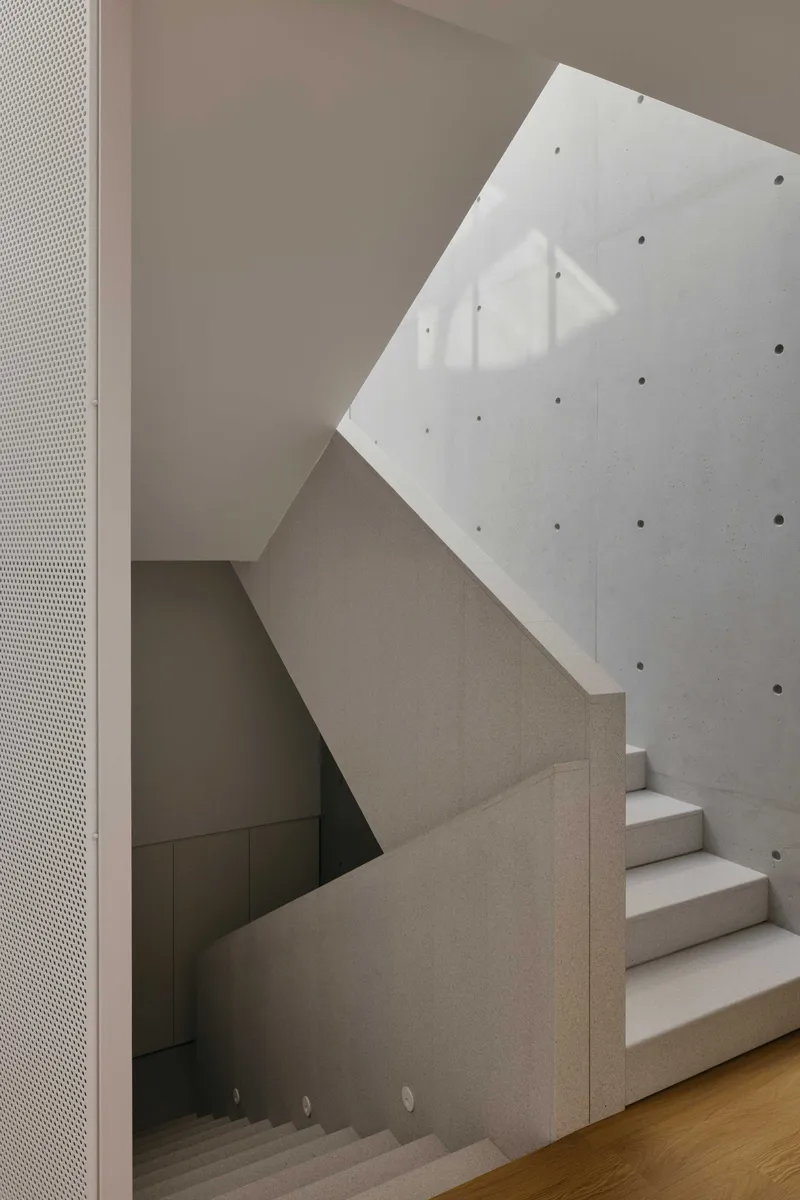 Concrete staircase with cantilevered treads beneath an angled skylight casting shadow patterns