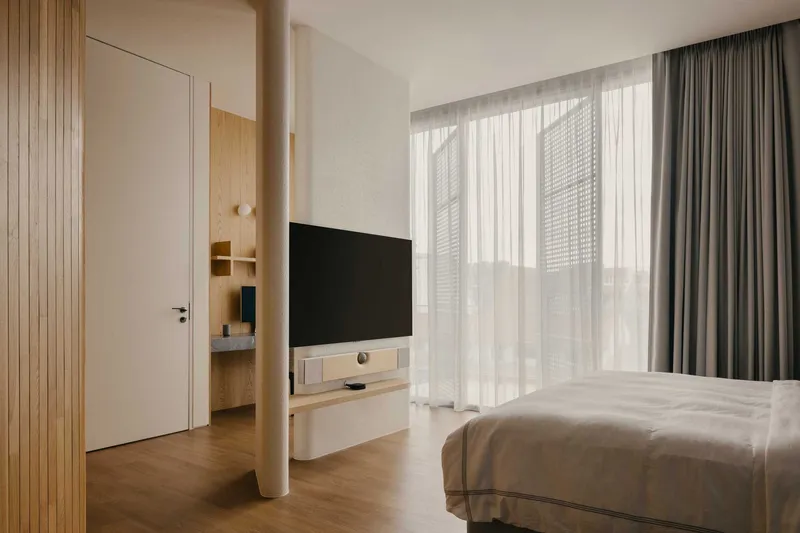 Bedroom with light timber paneling, sheer curtains, and a wall-mounted television opposite the bed