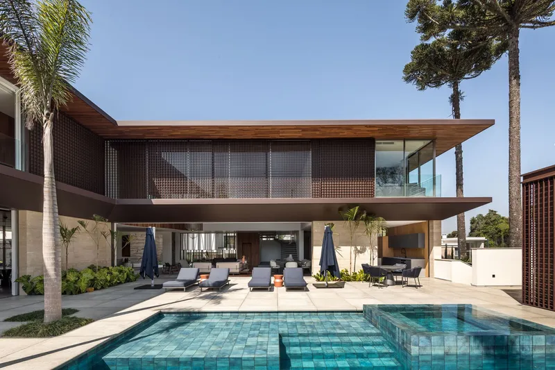 Pool terrace view showing cantilevered upper level with timber eaves and perforated metal screens flanked by palm trees