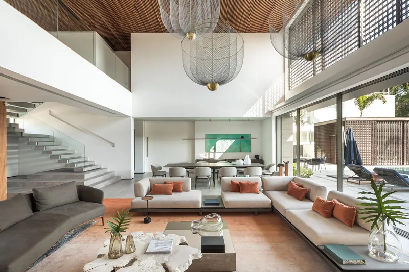 Double-height living room with floating staircase, timber slat ceiling and wire mesh pendant light fixtures at midday