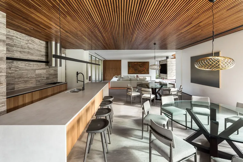 Kitchen and dining area with timber slat ceiling, concrete floor and glass balustrade overlooking the living space