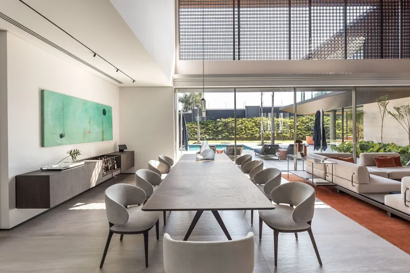 Long dining table beneath perforated metal screens and track lighting with pool view