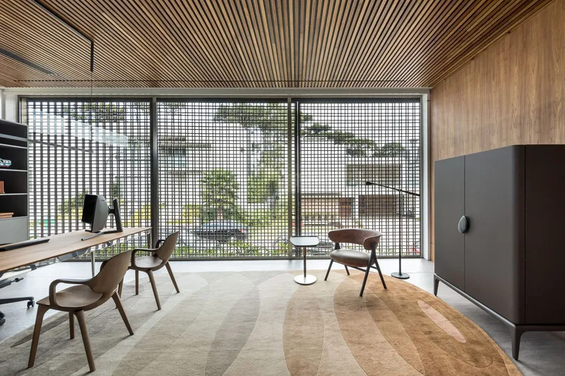 Interior study with radiating timber slat ceiling above a gridded metal screen wall opening to greenery